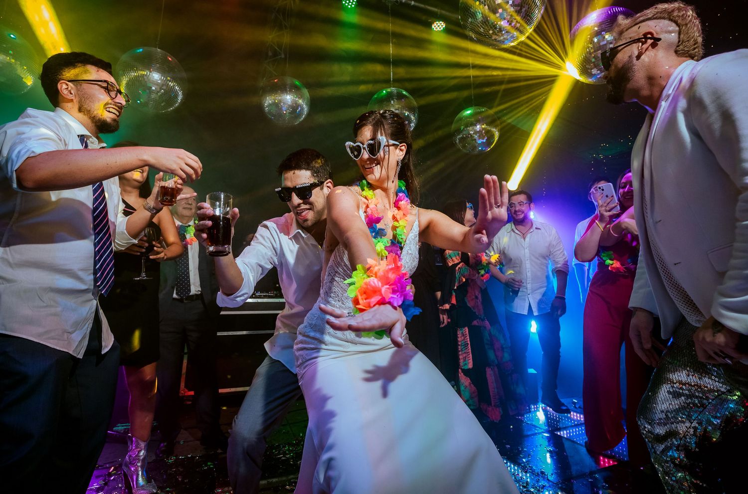 Bride and groom dancing at colorful wedding reception with disco balls and neon lights.