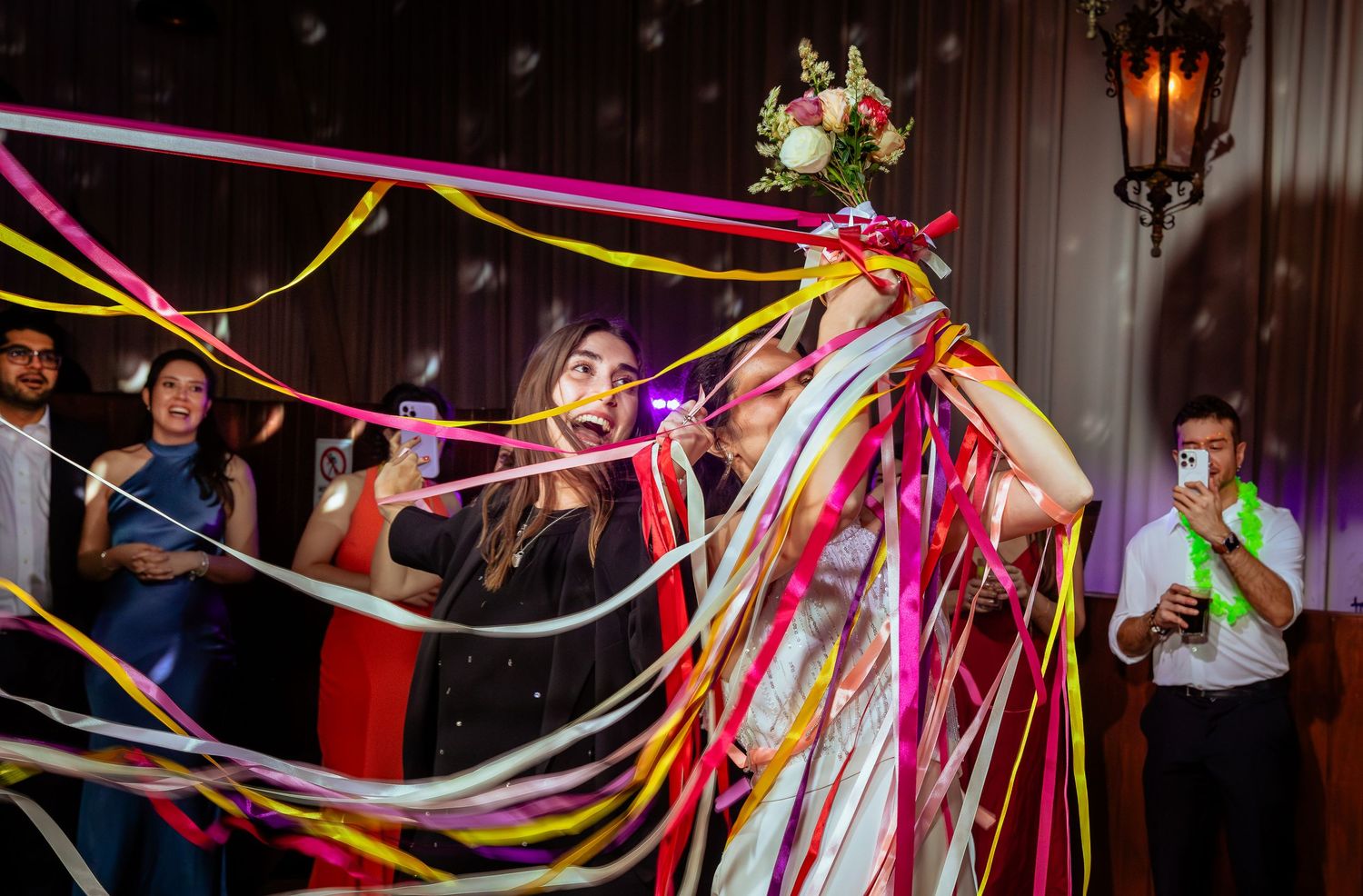 Bride laughing as colorful streamers wrap around her at festive wedding reception.