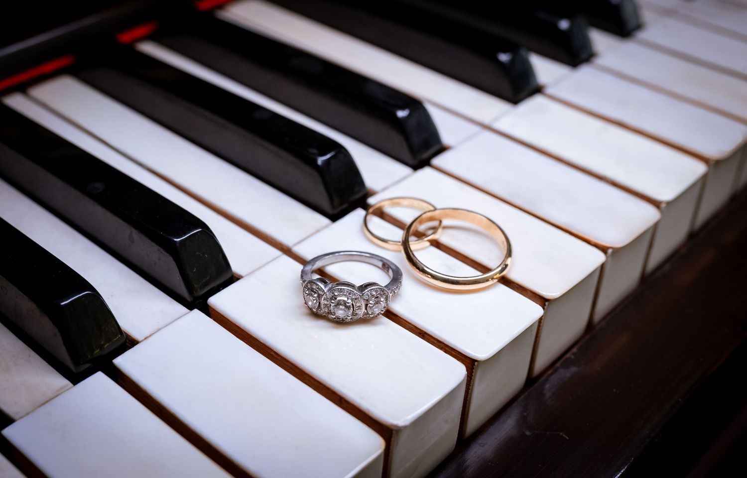 Two gold wedding bands and a diamond engagement ring resting on piano keys.