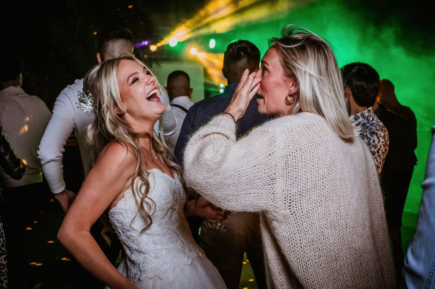 Laughing bride in white gown shares joyful moment with female guest on wedding dance floor.