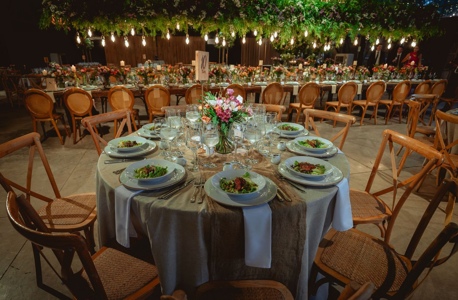 Elegant outdoor wedding reception with round tables, string lights, and floral centerpieces.