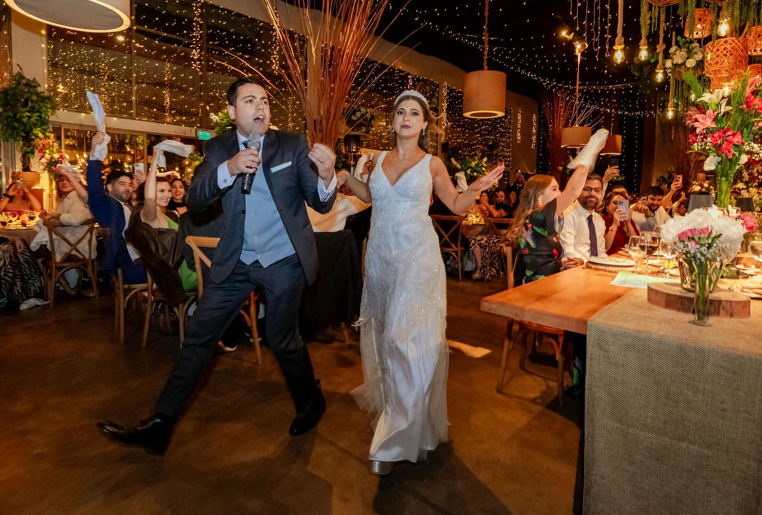 Excited bride and groom celebrating their wedding reception entrance with cheering guests behind them.