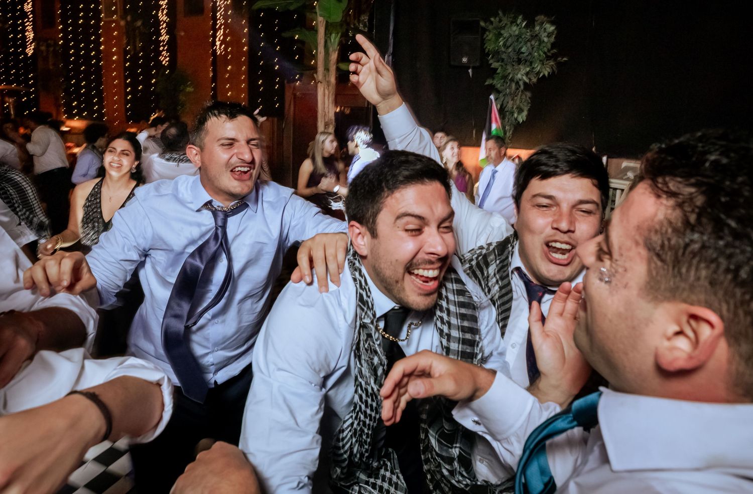 Group of cheerful male wedding guests laughing and embracing together at a lively reception party.