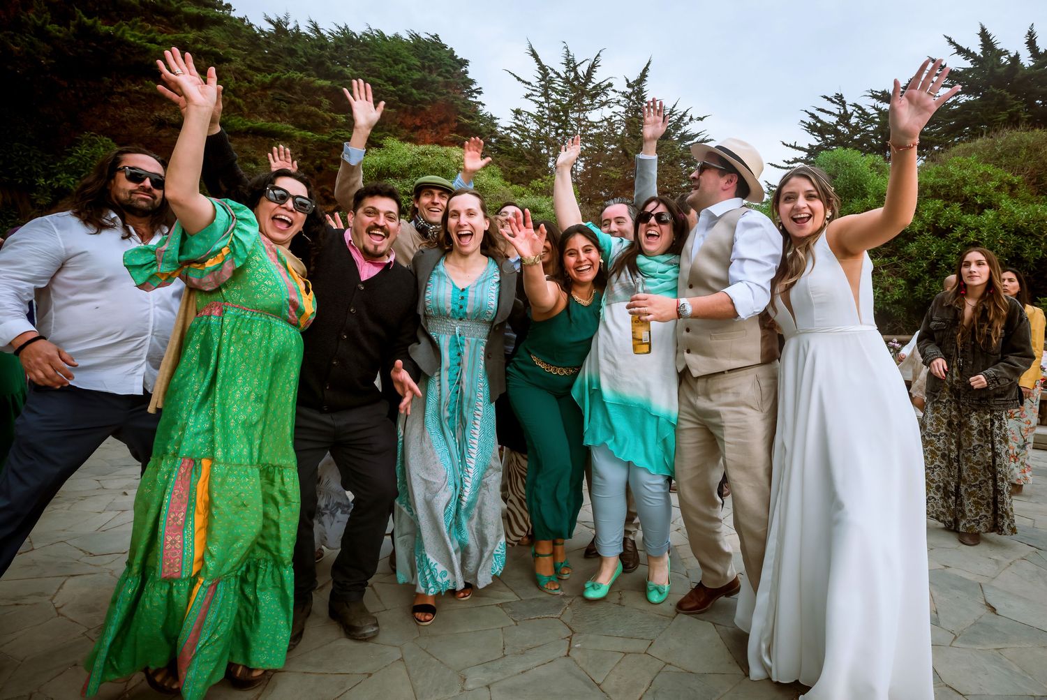 Joyful wedding guests in colorful outfits cheering with bride in white dress outdoors.