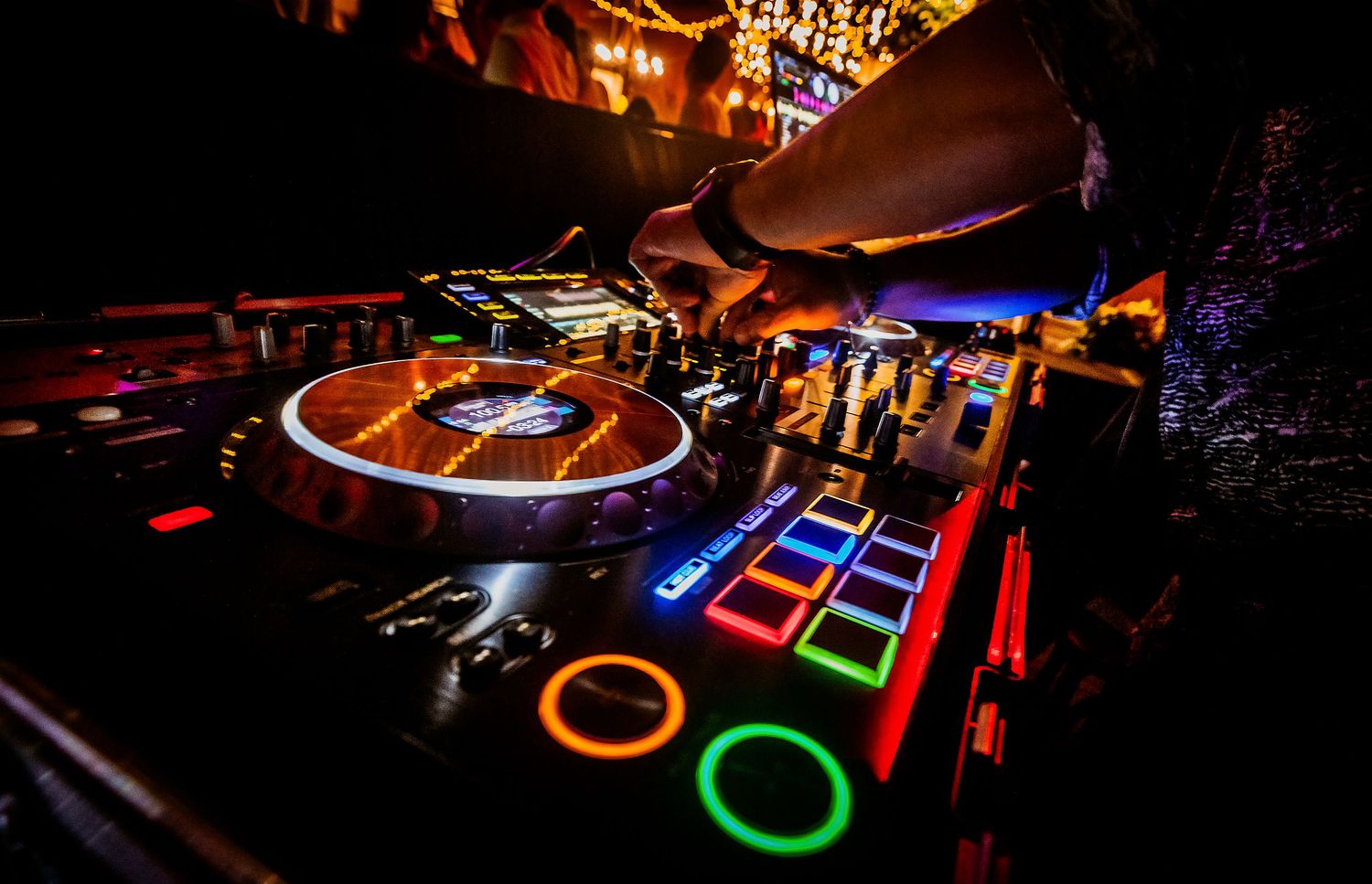 DJ equipment with colorful glowing pads and turntable in a vibrant nightclub setting.