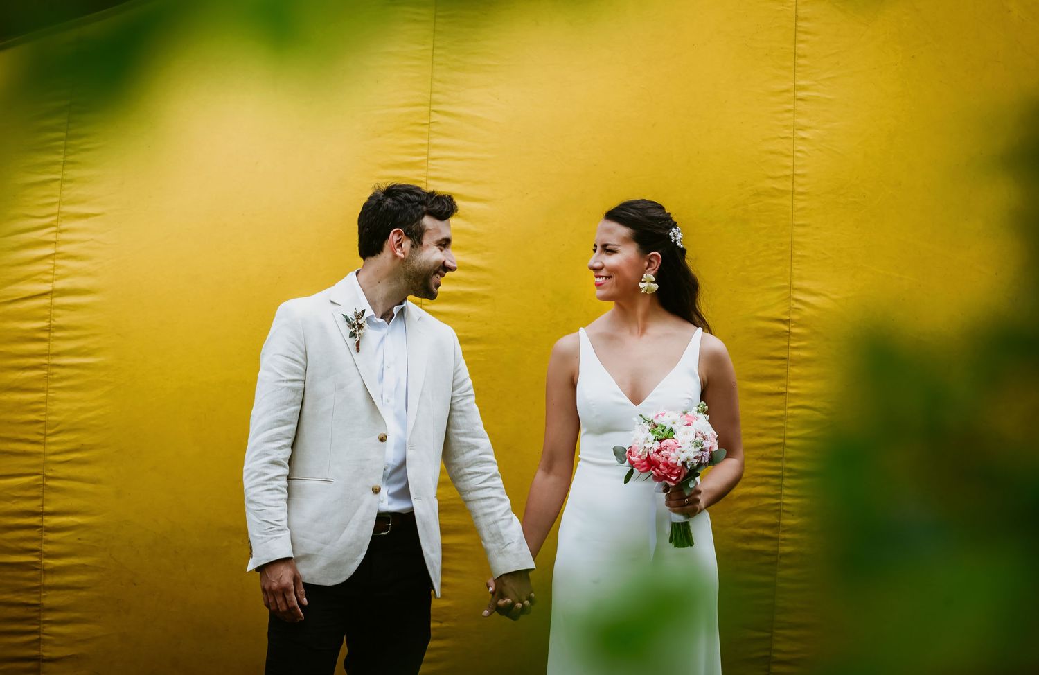 Bride and groom sharing a joyful moment in front of a golden backdrop outdoors.