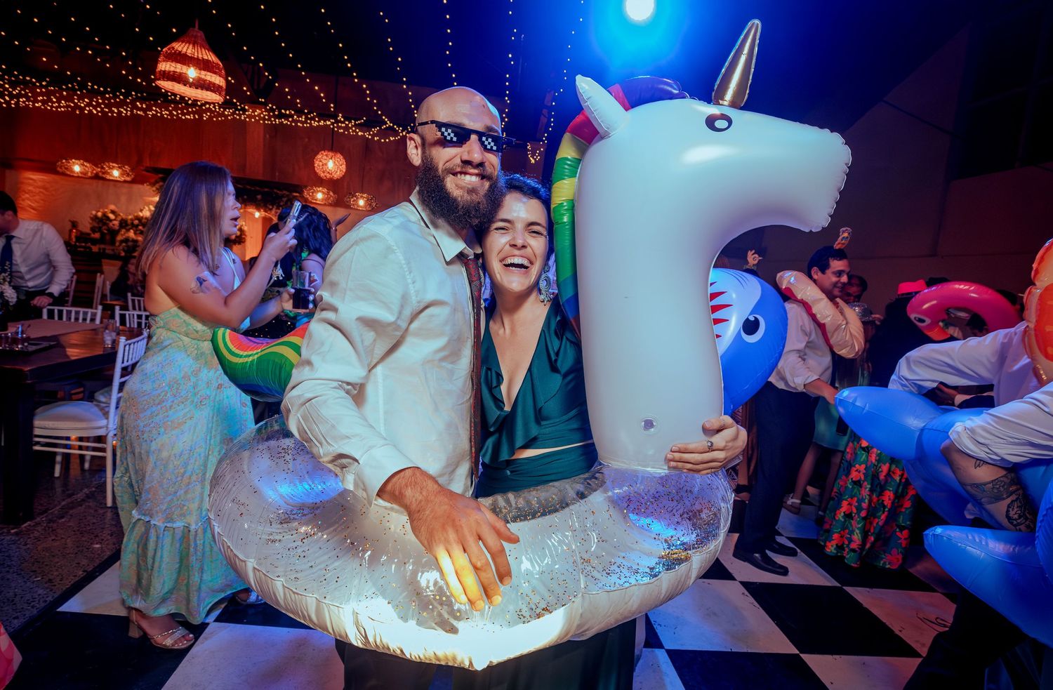 Bearded man and woman pose with inflatable unicorn float at fun wedding party.