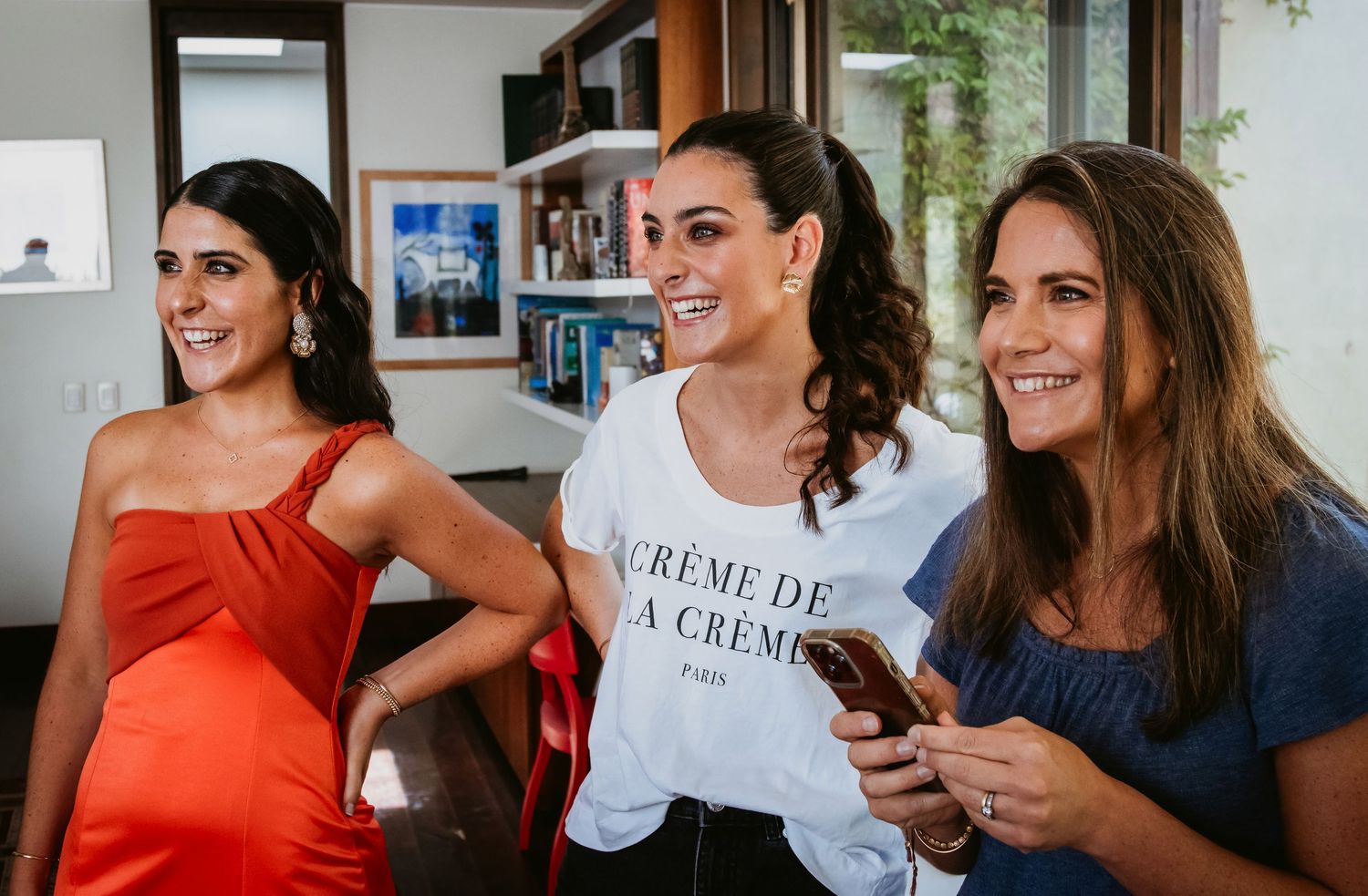 Three women laughing together at a wedding celebration wearing elegant dresses.