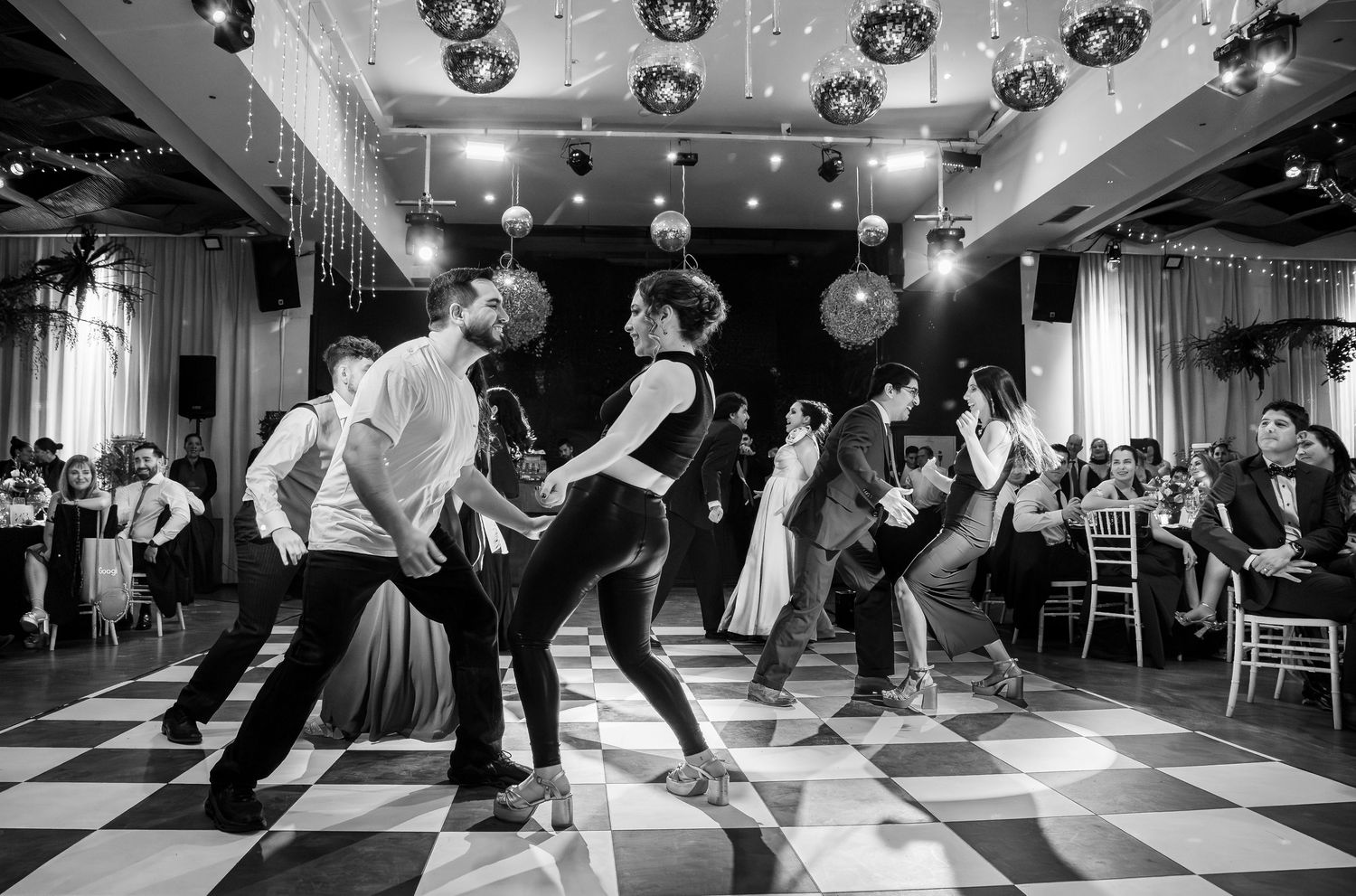 Wedding guests perform synchronized dance routine on black and white checkered ballroom dance floor.