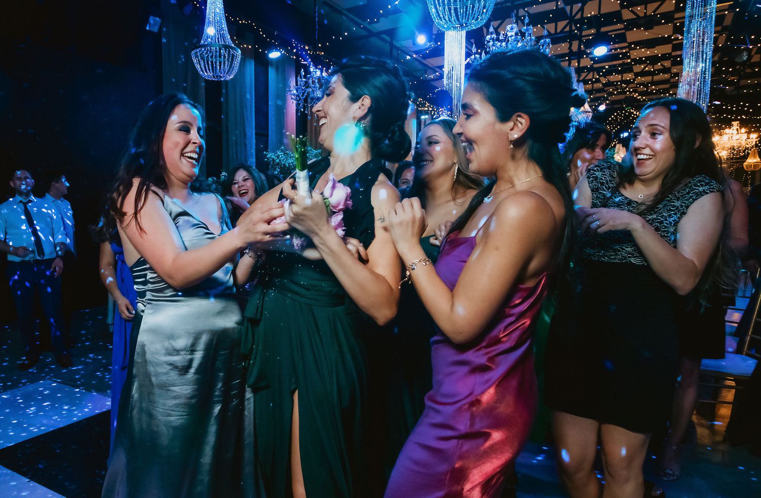 Women in elegant dresses laughing and dancing together at a wedding reception party.