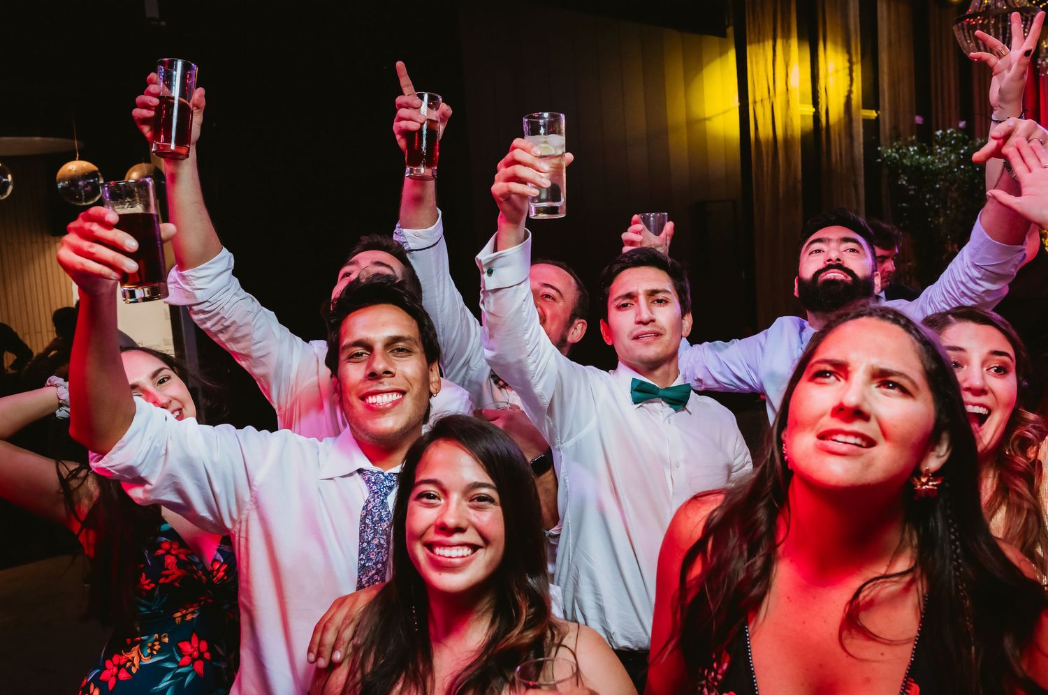Smiling wedding guests raising glasses in a toast at a festive reception celebration.