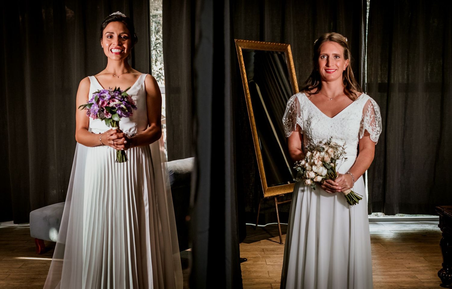 Two brides in white gowns holding bouquets stand smiling in front of a mirror.