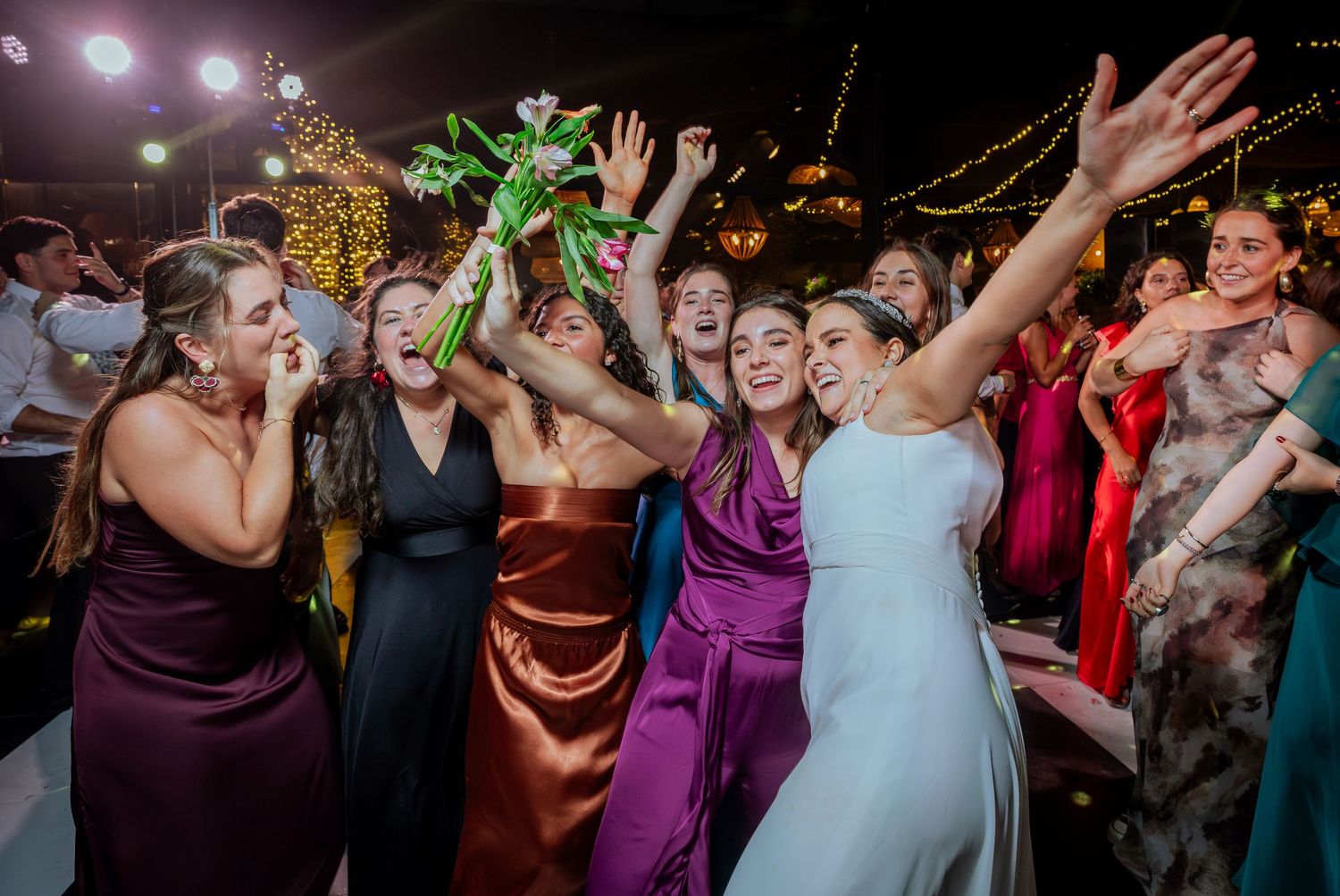 Bride and bridesmaids laugh and celebrate during bouquet toss at wedding reception.