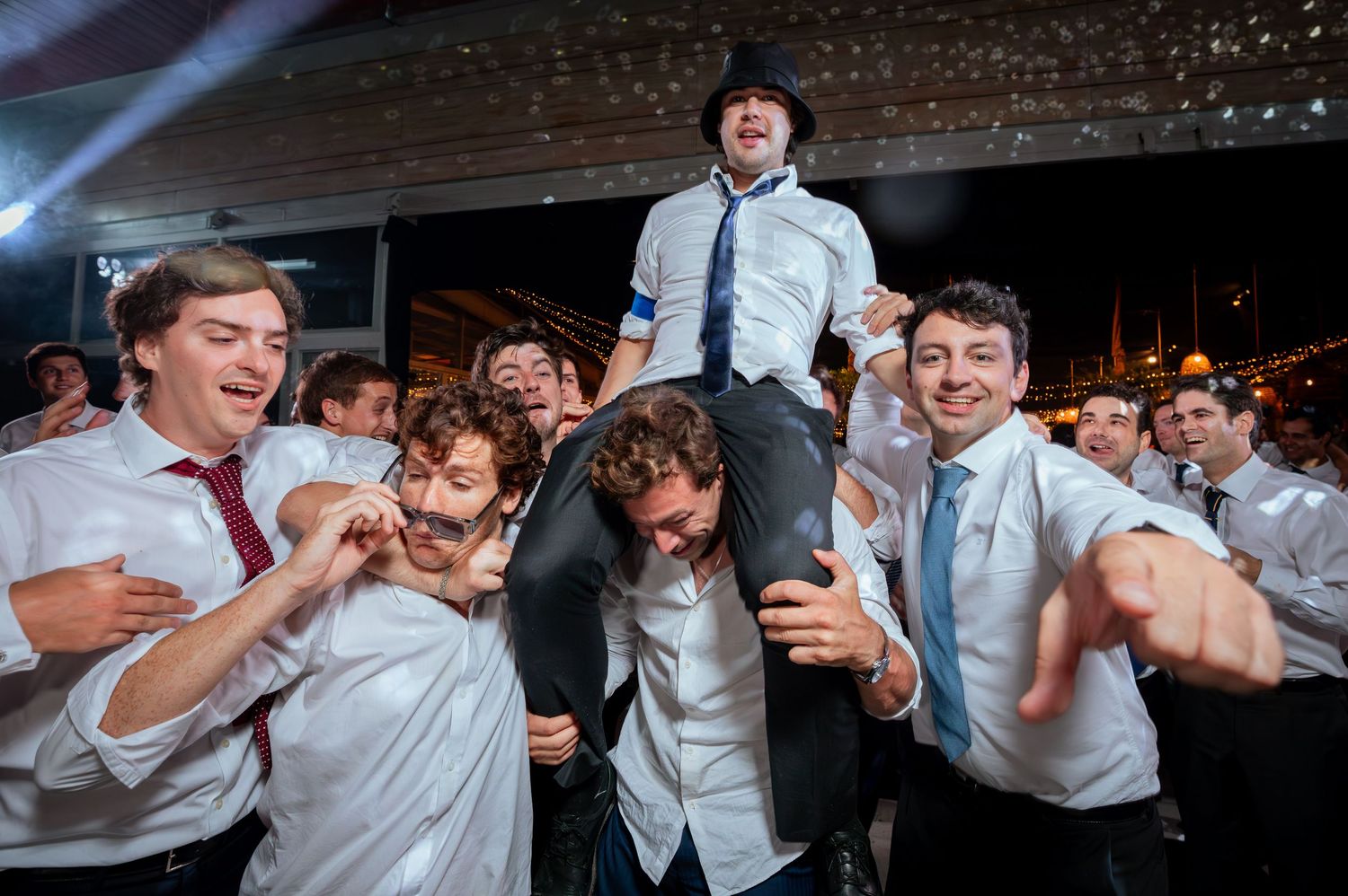 Groomsmen celebrate as they lift groom on shoulders at festive wedding reception.