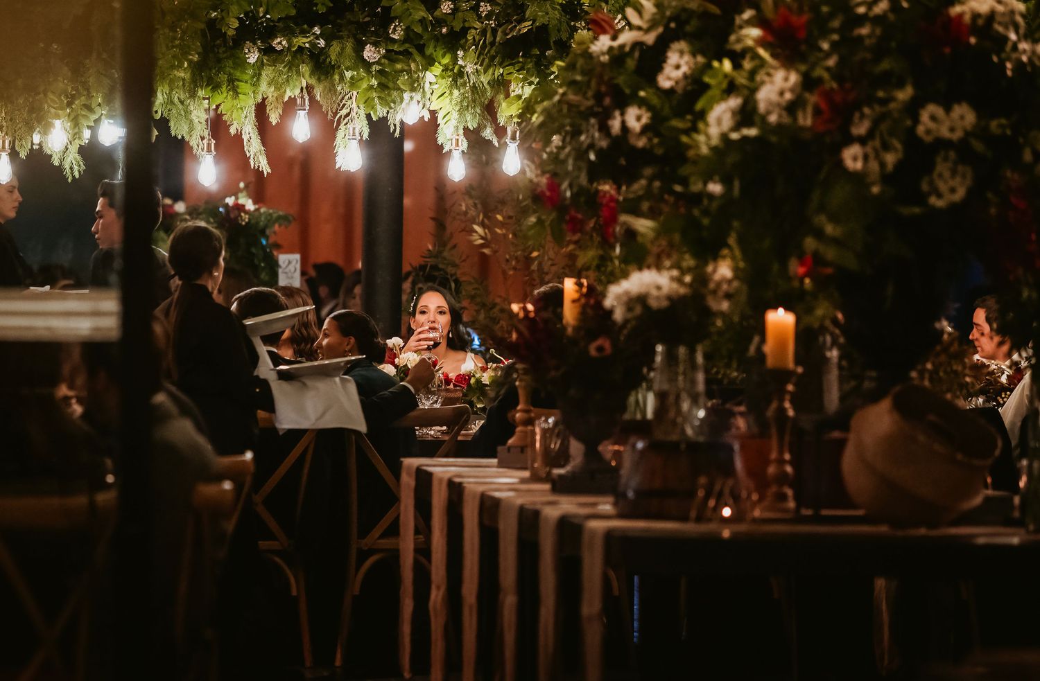 Elegant candlelit wedding reception with floral arrangements, string lights, and guests dining at a decorated long table.