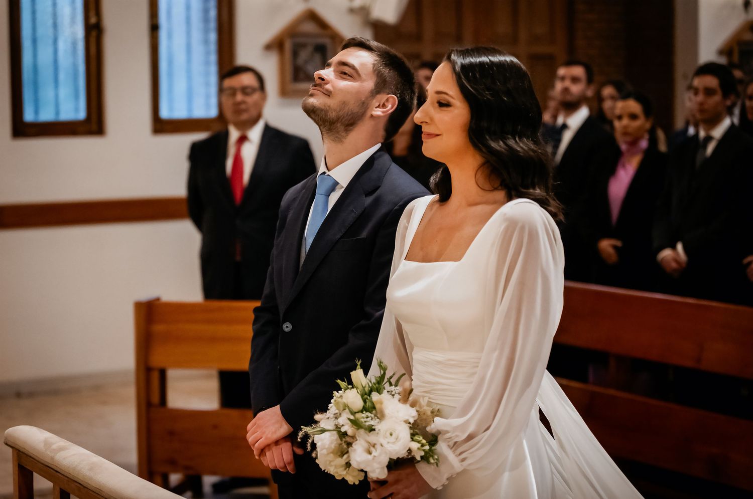 Bride and groom standing at church altar during wedding ceremony, bride holding white bouquet.