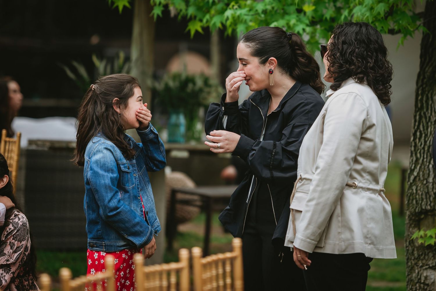 Two women and a girl share an emotional moment laughing outdoors at a garden event.