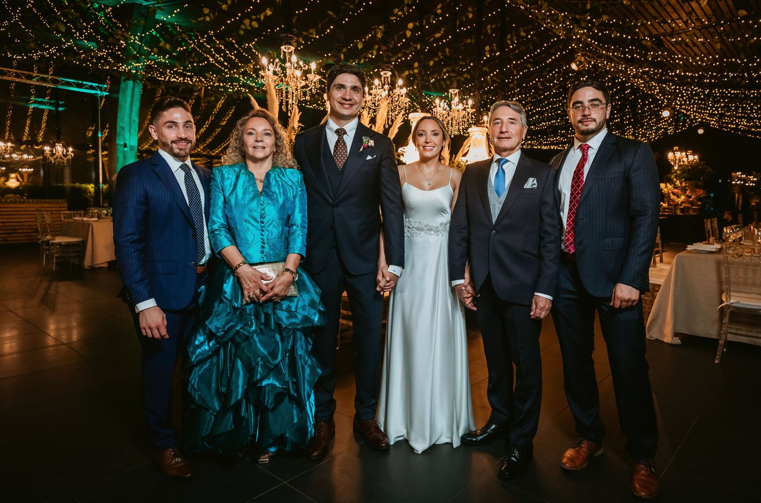 Wedding group photo of six people posing under fairy lights at elegant reception.