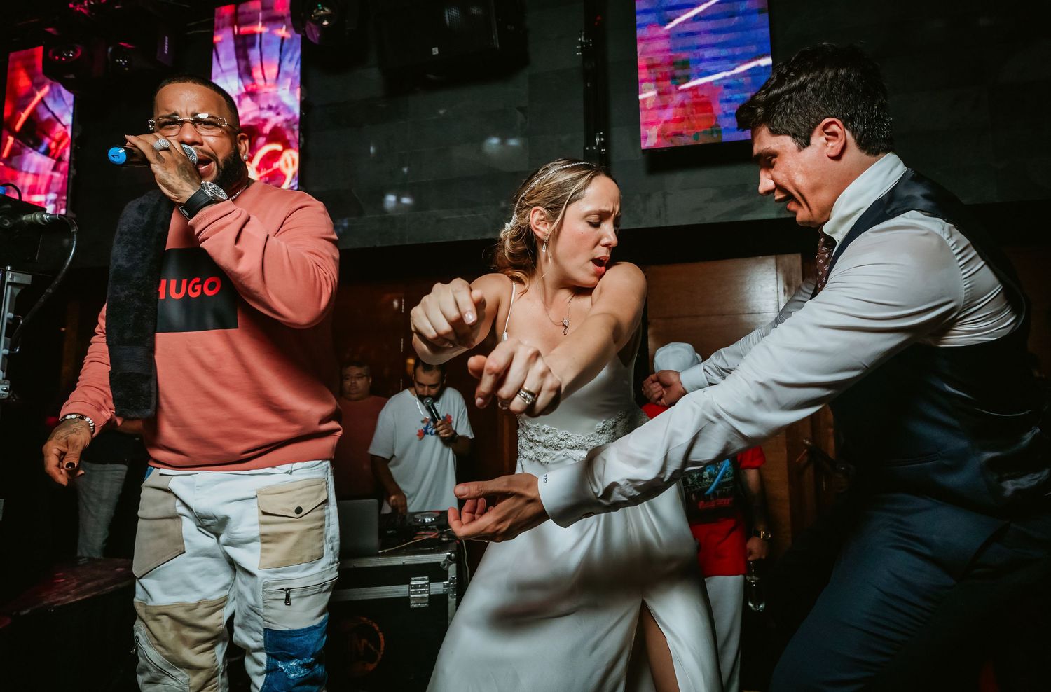 Performer in Hugo sweatshirt dancing with bride and groom at exciting wedding reception.
