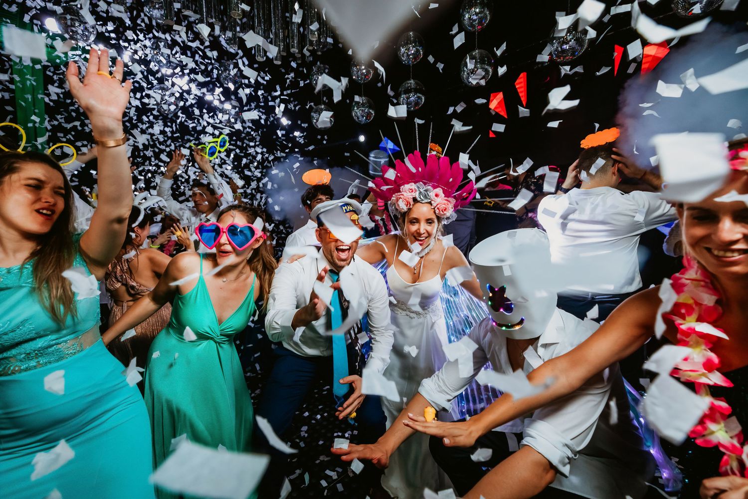 Colorful confetti rains over dancing wedding guests in festive costumes at an energetic wedding reception party.