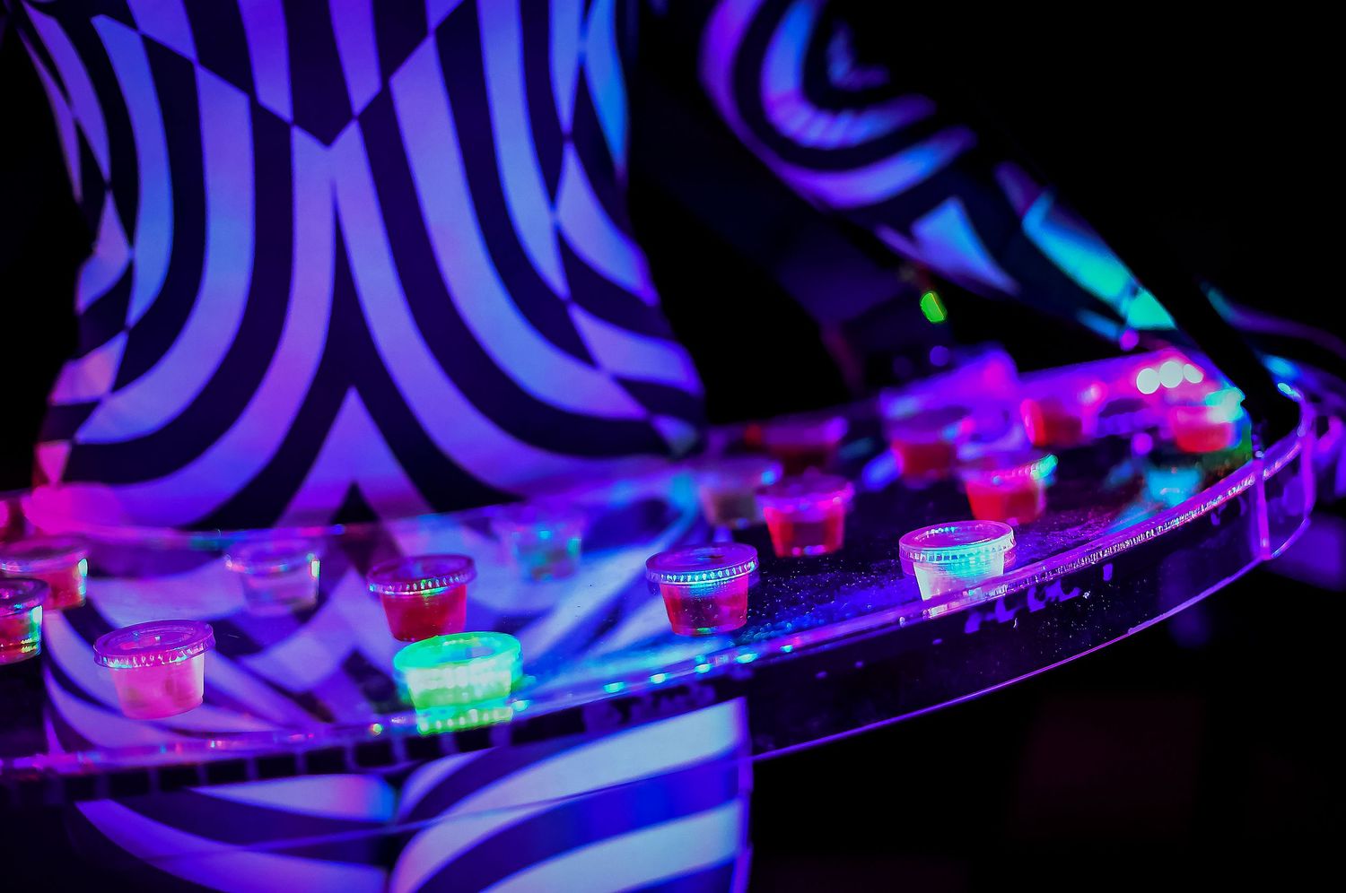 Glowing neon shot glasses on a tray held by a zebra-print server at a nightclub event.