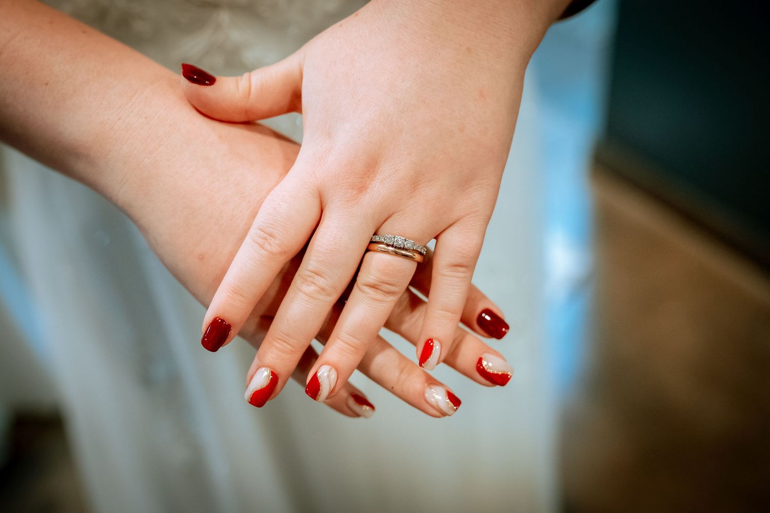 Two brides hold hands showing engagement rings and red nail polish on their wedding day.