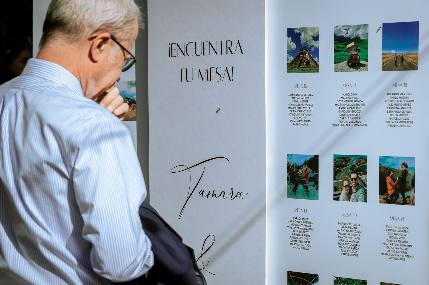 Wedding guest reviewing seating chart display board named Tamara with couple photos at reception.