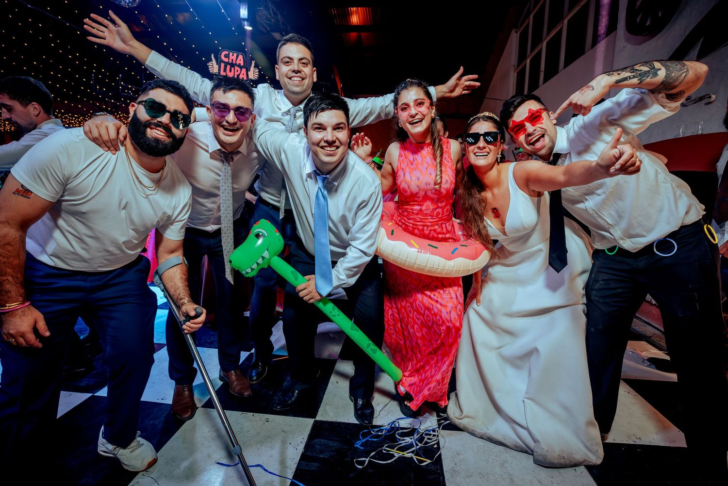 Wedding party posing with inflatable props on a checkered dance floor at a lively reception celebration.