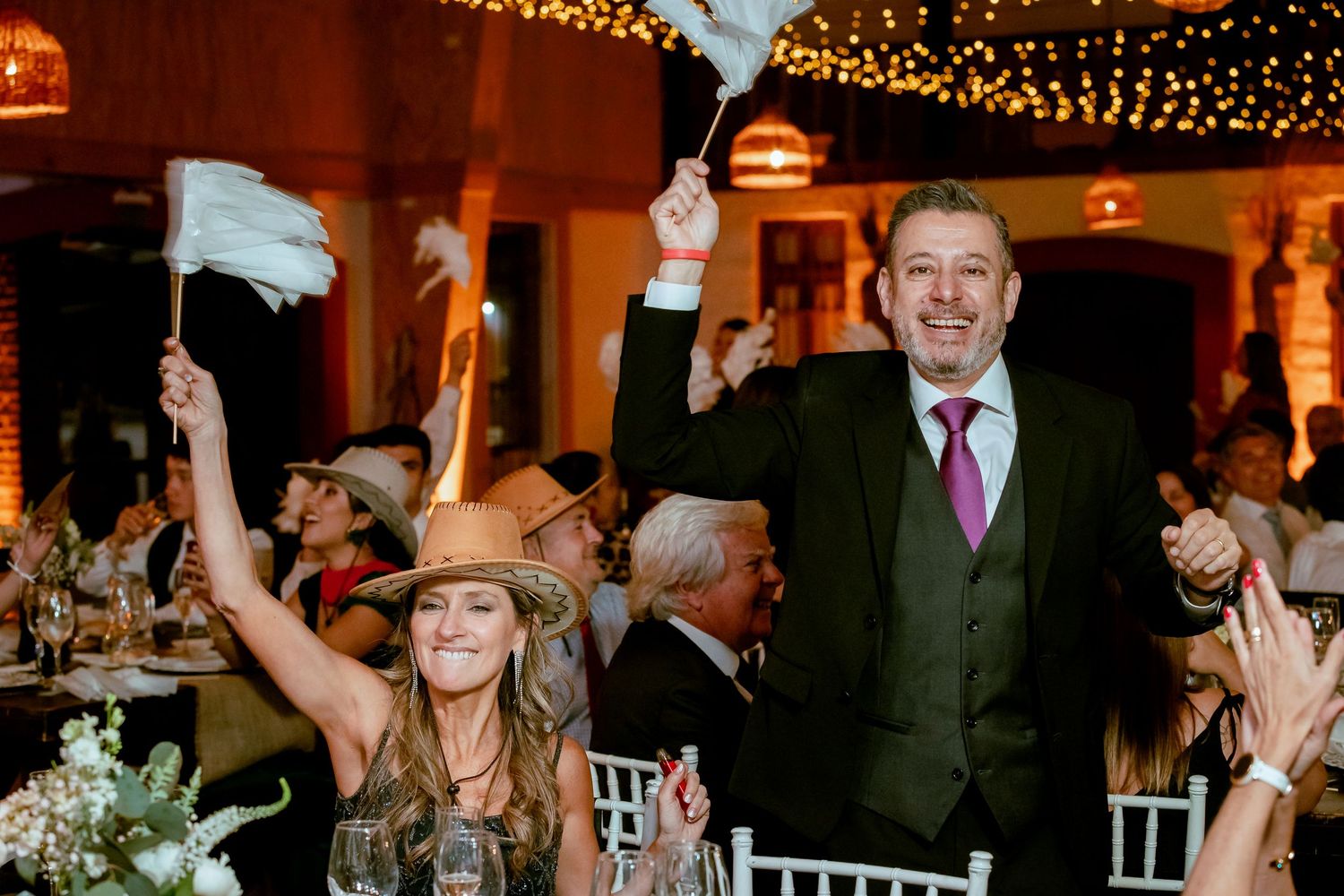 Wedding guests wave white flags and celebrate at romantic candlelit reception dinner.