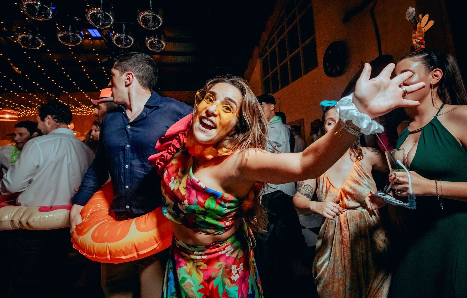 Woman in colorful floral dress dancing energetically with guests at a festive wedding reception party.