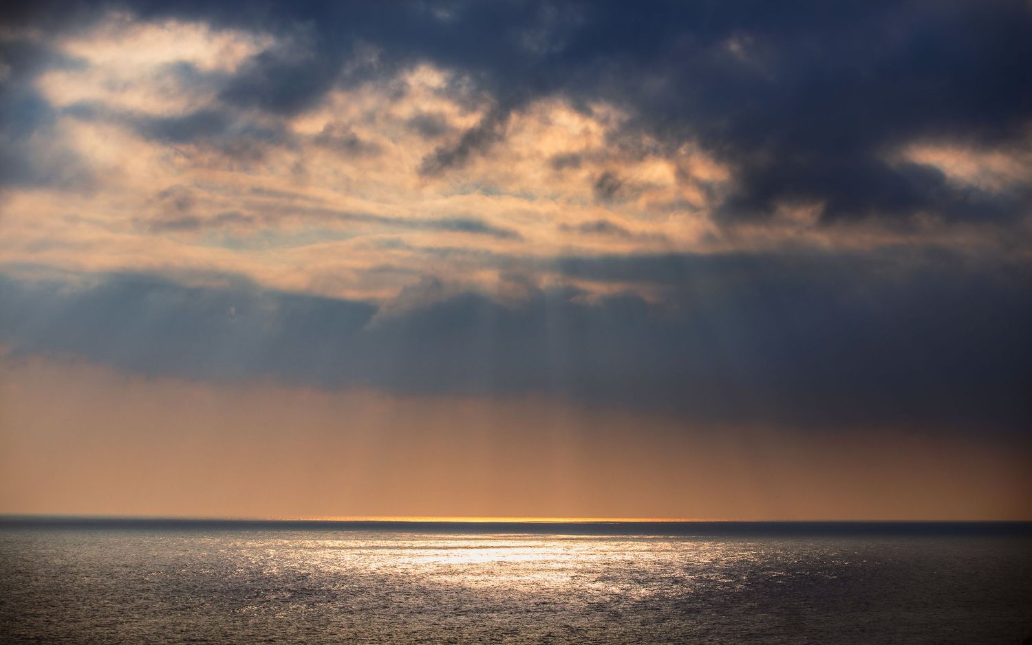 Dramatic ocean sunset with rays of light breaking through stormy clouds.