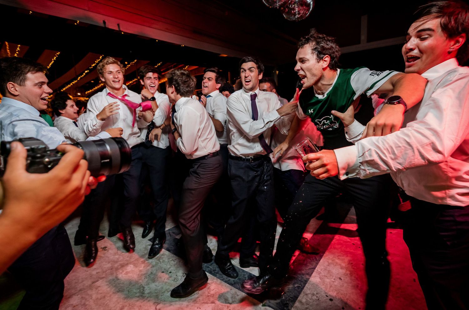 Energetic group of men in suits celebrate and dance wildly together at a wedding reception party.