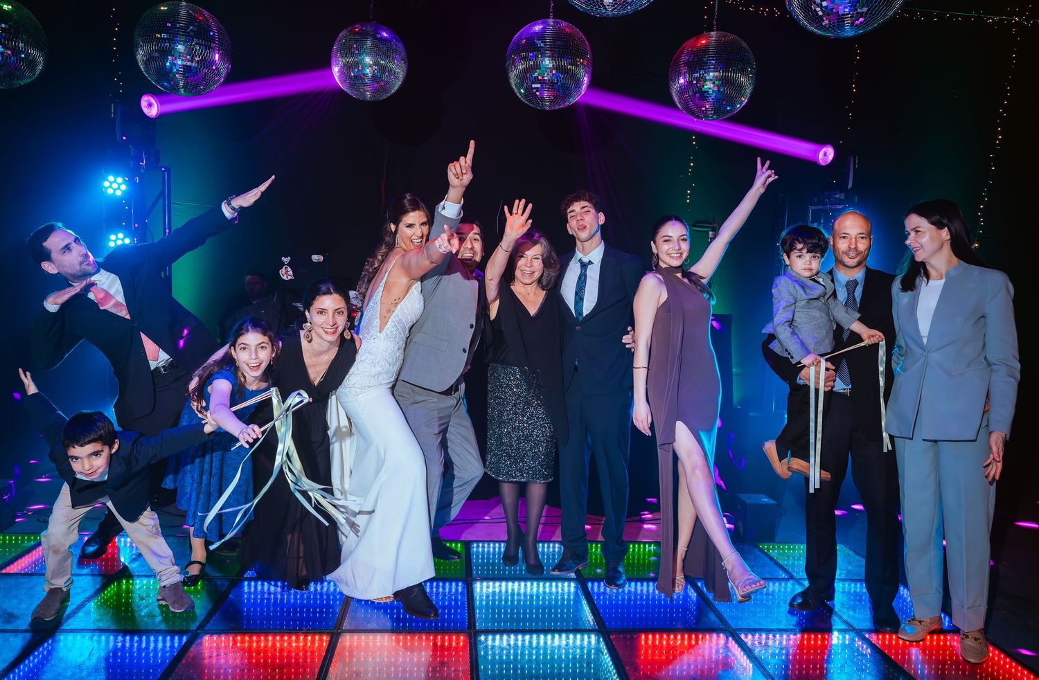 Group of people posing on a colorful dance floor under disco balls at a lively party event.