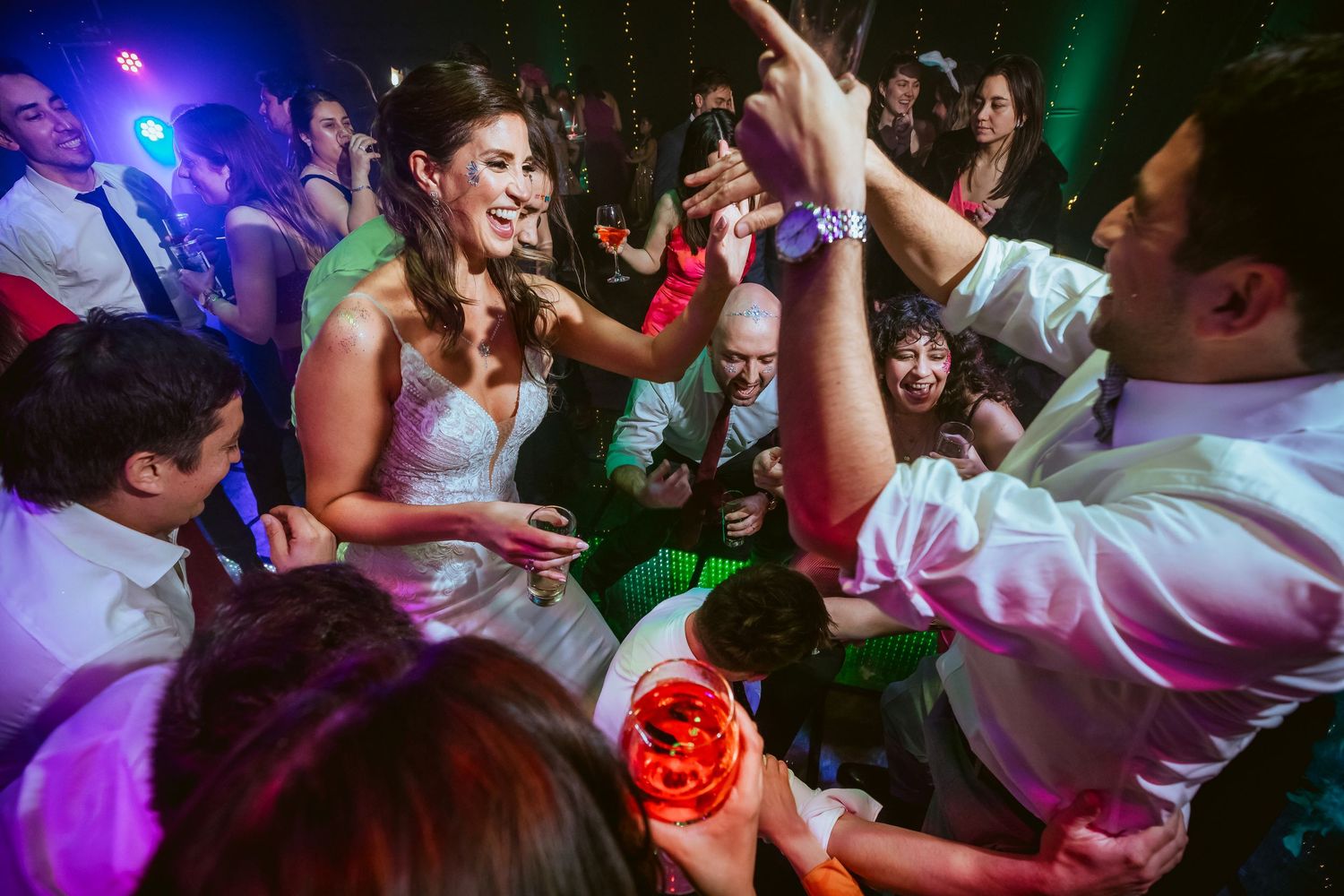 Bride and guests dancing joyfully at a lively wedding reception party with colorful lights.