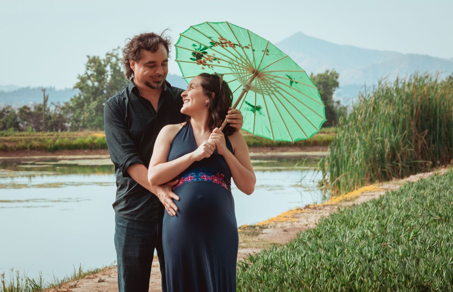 Happy couple sharing a moment under a green parasol by a tranquil lake.