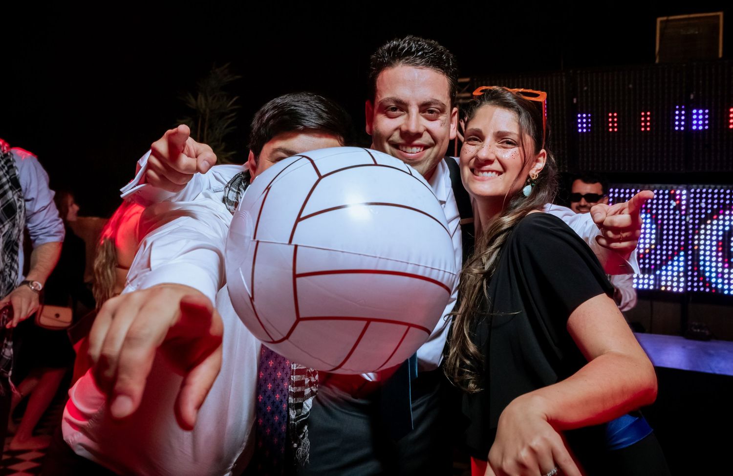 Smiling wedding guests pose with an inflatable volleyball ball at a festive reception celebration.