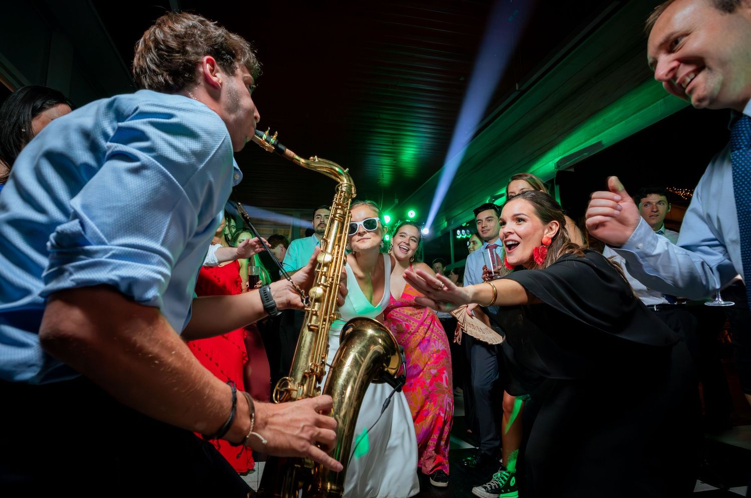 Saxophonist serenades excited wedding guests in colorful dresses on the dance floor.