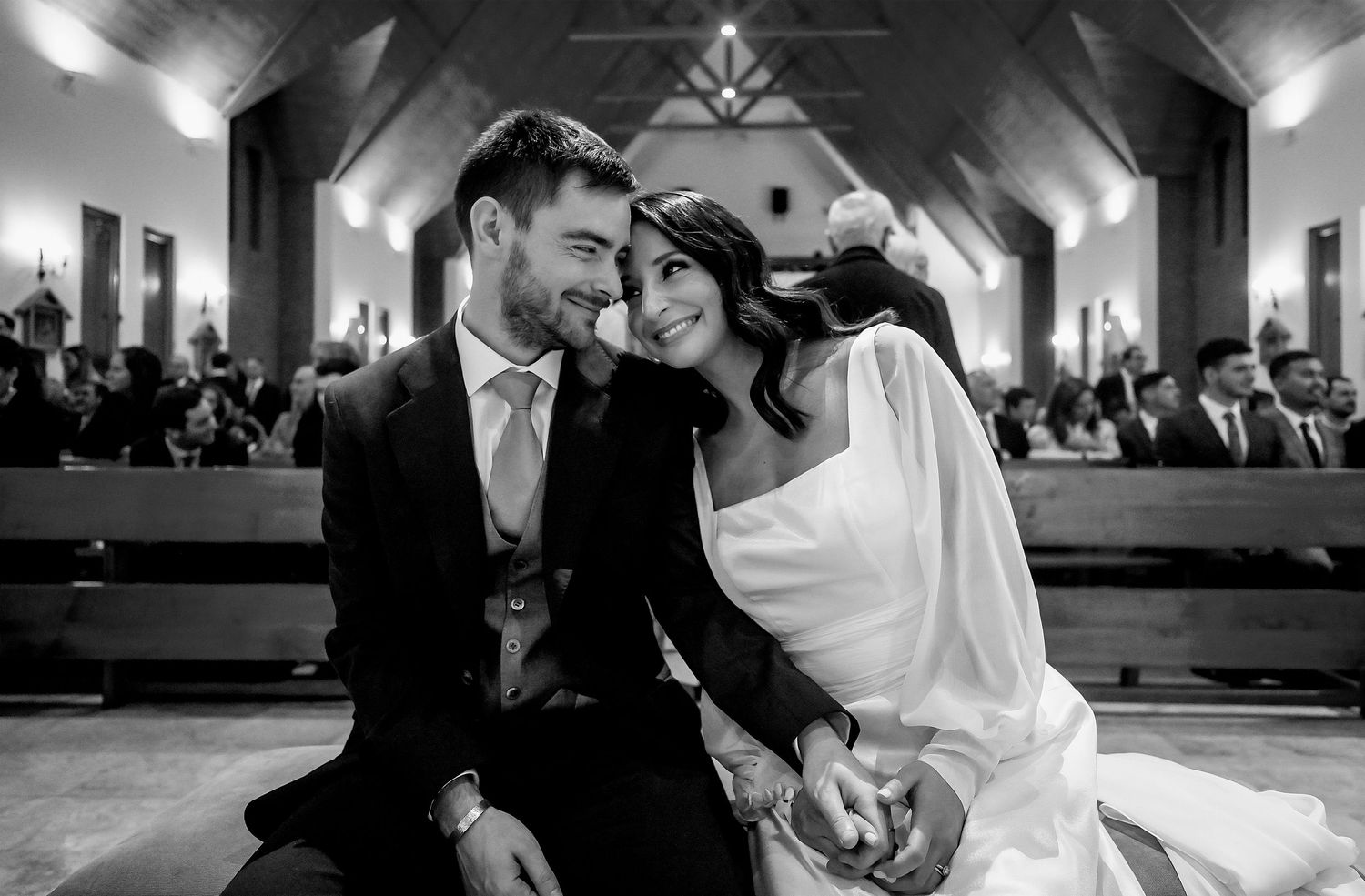 Black and white wedding photo of bride and groom sharing an intimate moment seated in a church.