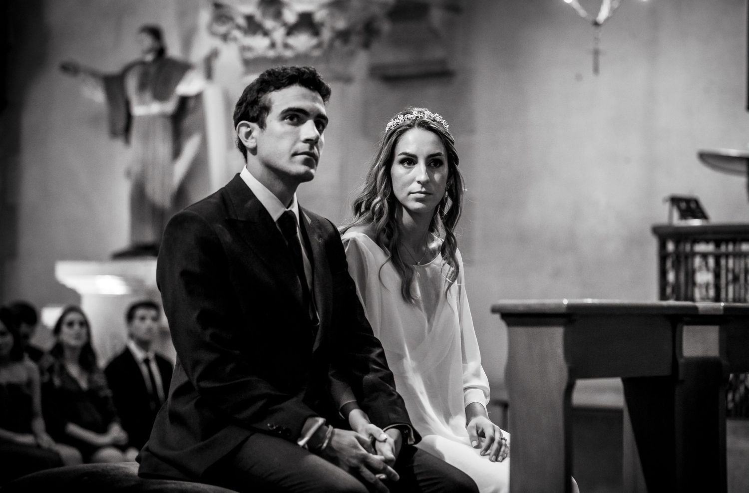 Black and white close-up of bride and groom seated together during church wedding ceremony.