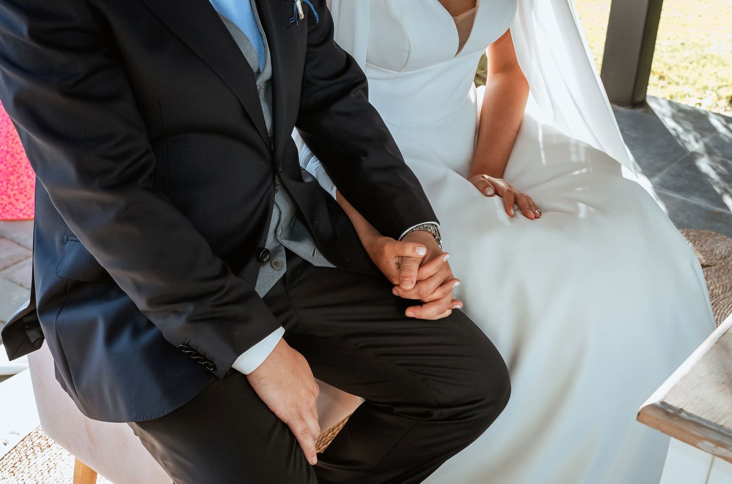 Bride and groom hold hands tenderly while seated together during their wedding ceremony.