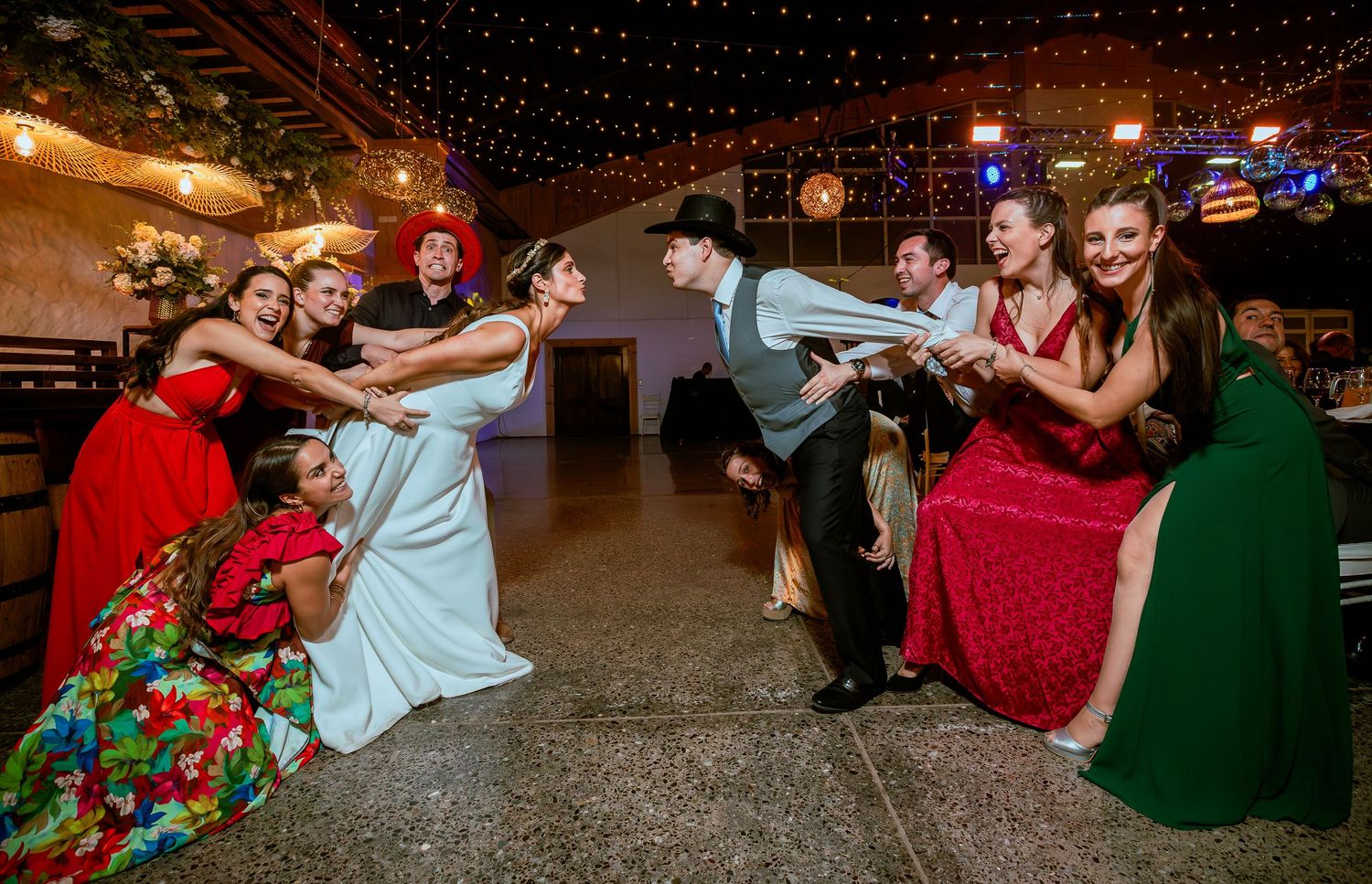 Bride and groom play tug-of-war with wedding guests on dance floor at festive reception.
