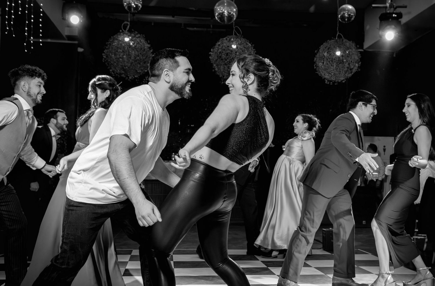 Guests dance energetically together on checkered floor at lively wedding reception celebration.