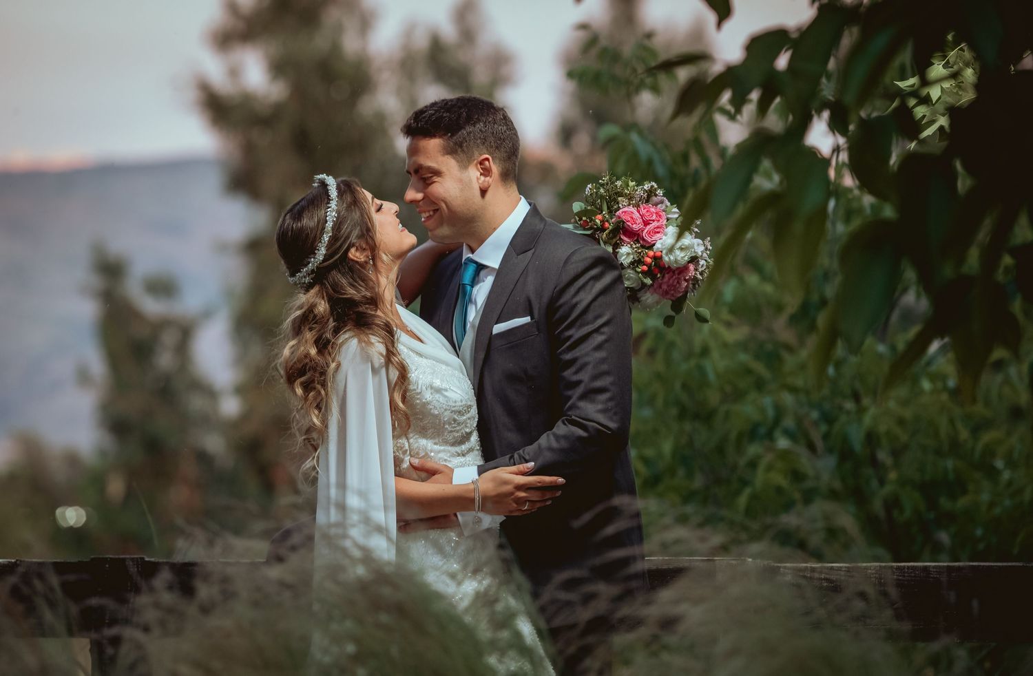 Bride and groom share a tender moment gazing at each other surrounded by vibrant green foliage.