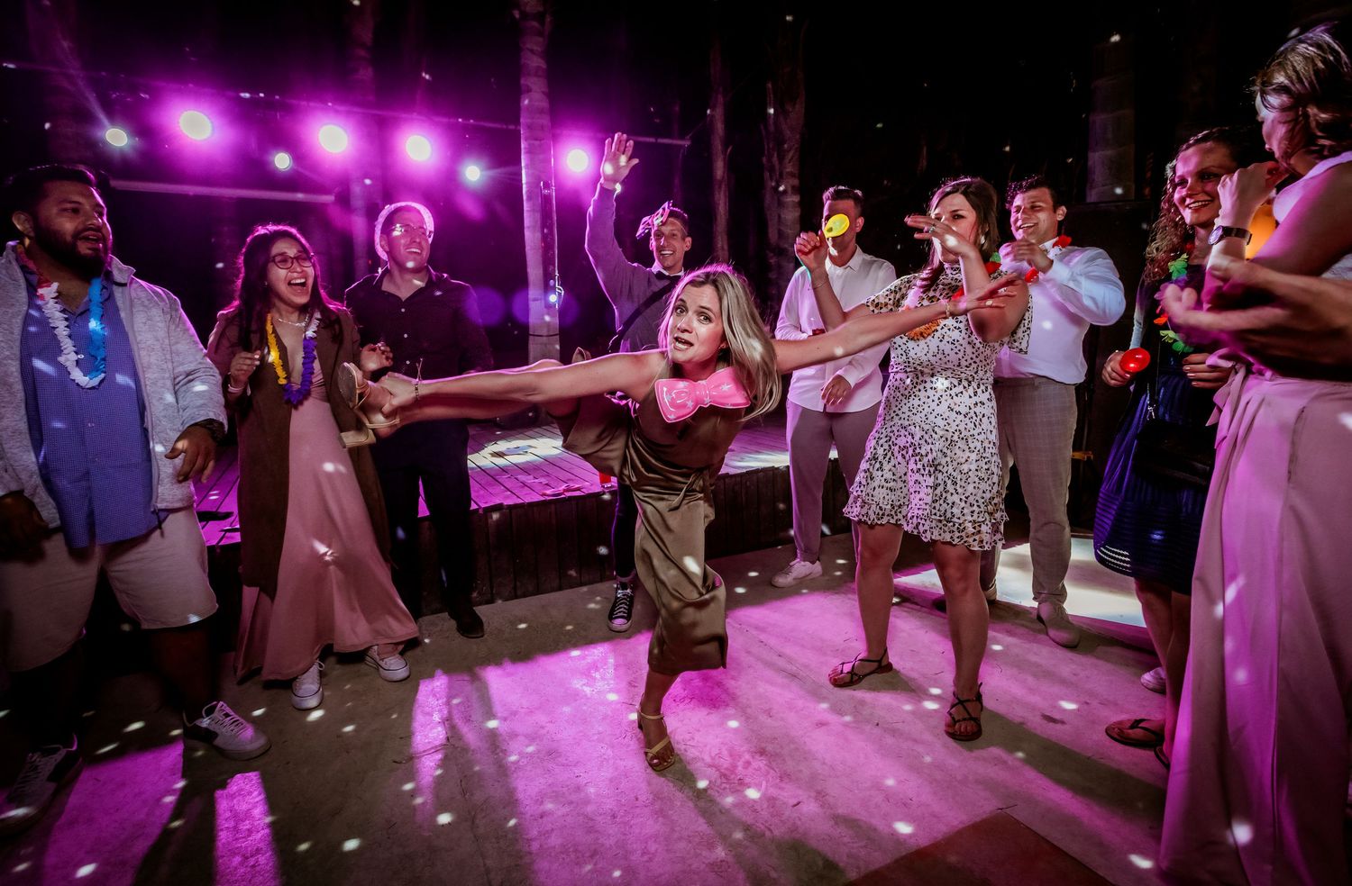 Bride in gold dress spins on dance floor surrounded by cheering wedding guests.