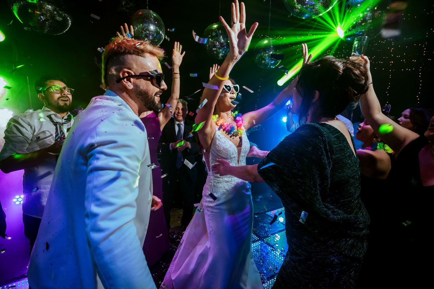 Bride and groom dancing joyfully at a vibrant wedding reception with colorful disco lights and confetti.