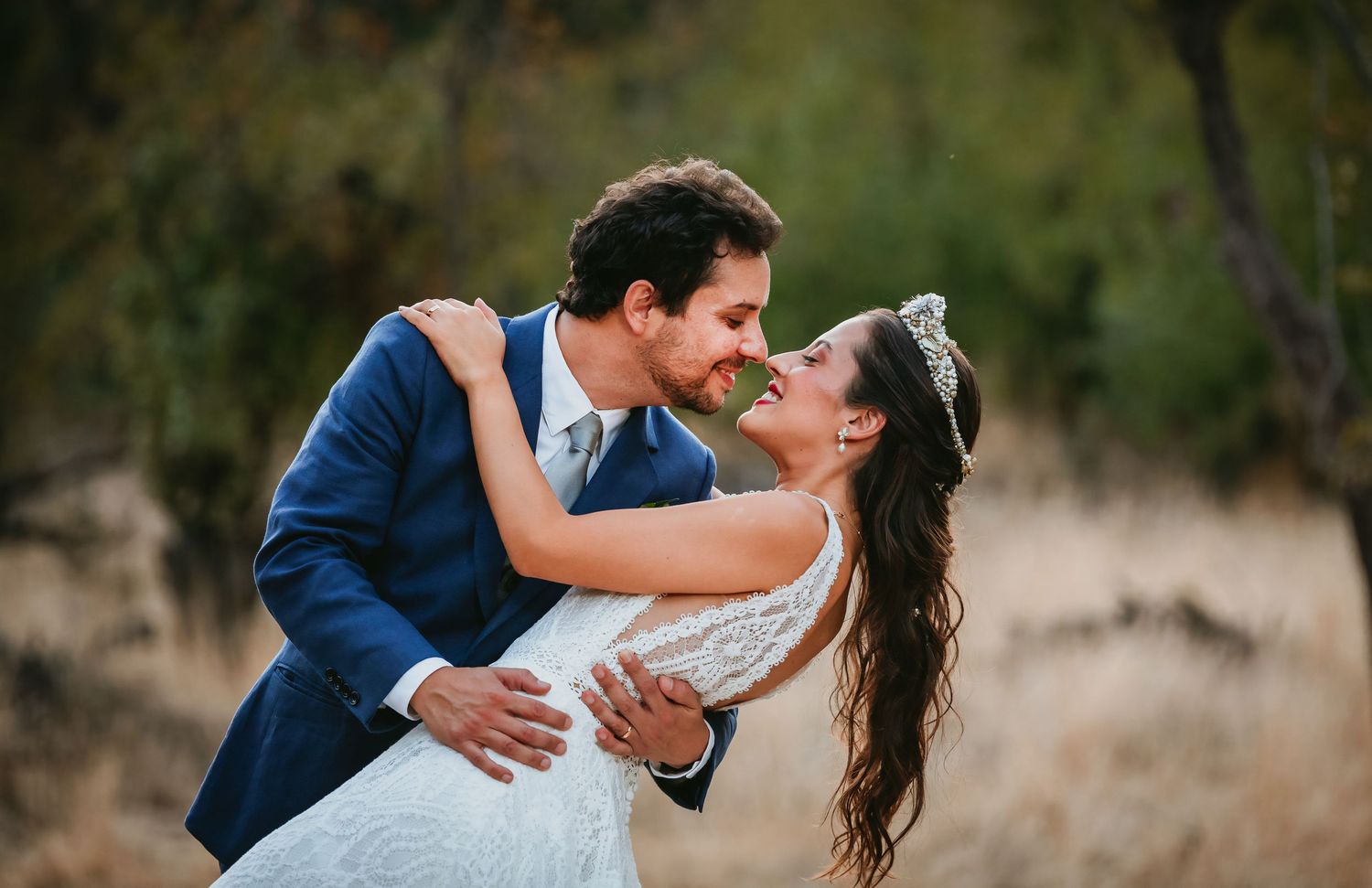 Groom dipping bride in a tender embrace in a golden field with trees in background.