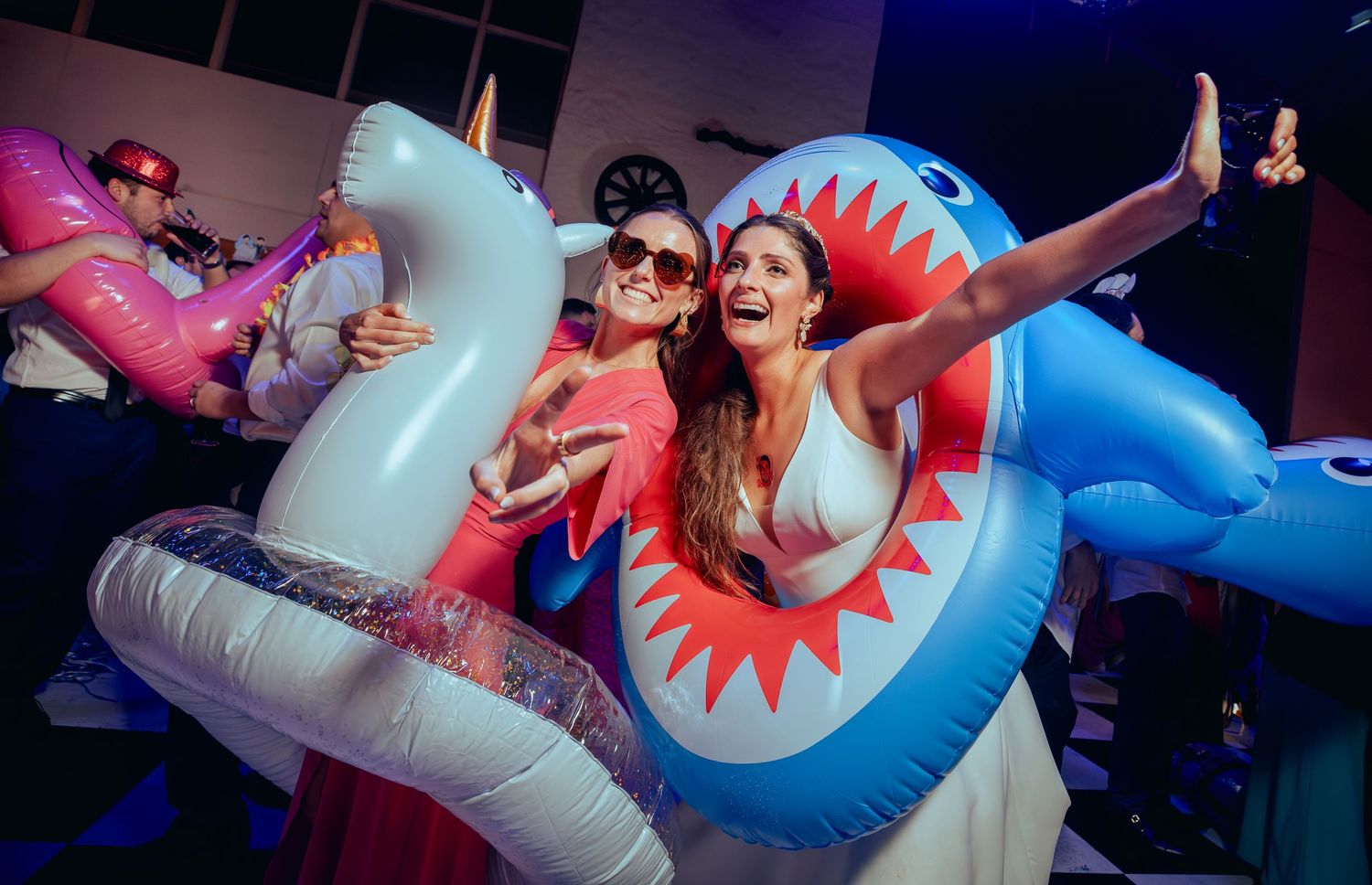 Three women posing with inflatable unicorn and shark pool toys at a festive wedding reception.