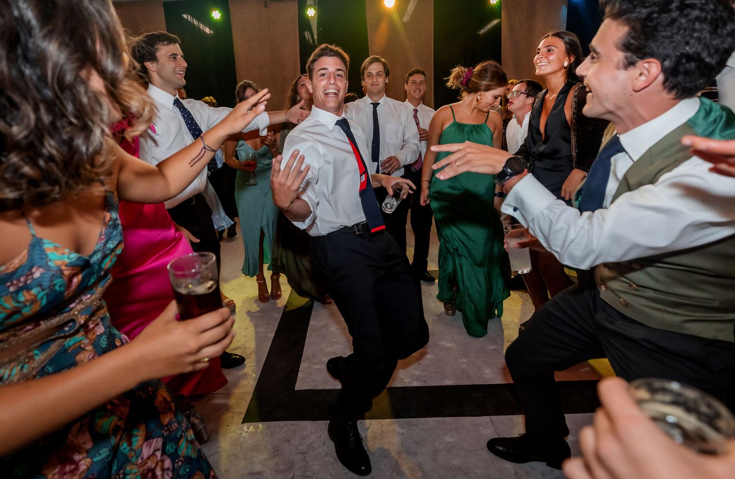 Energetic wedding guest dancing enthusiastically surrounded by cheering friends at a lively reception.