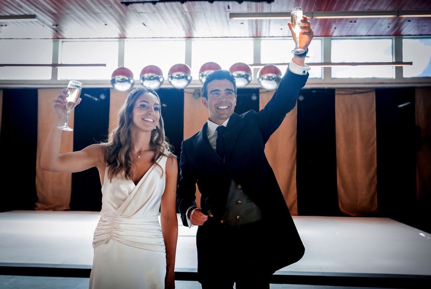 Bride and groom raising glasses in a celebratory toast on the wedding dance floor.