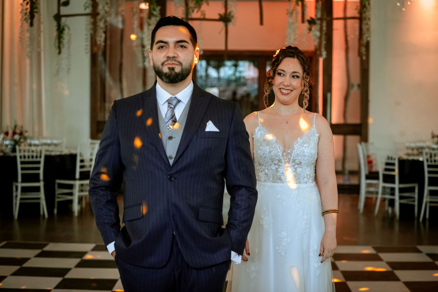 Bride and groom pose together in decorated wedding reception hall with black and white floor.